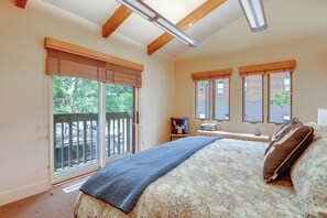 A bedroom with a large bed, a window with a view of greenery, and a ceiling fan.