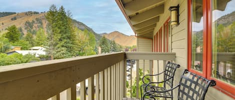 A wooden balcony with two metal chairs, a view of a parking lot, and a mountain in the background.