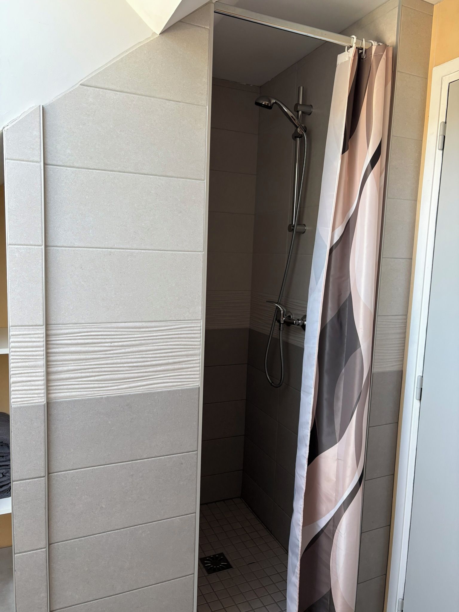 Un angolo doccia con tenda, soffione a mano e pavimento piastrellato.