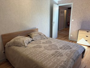 A bedroom with a bed, a nightstand, and a door leading to another room.