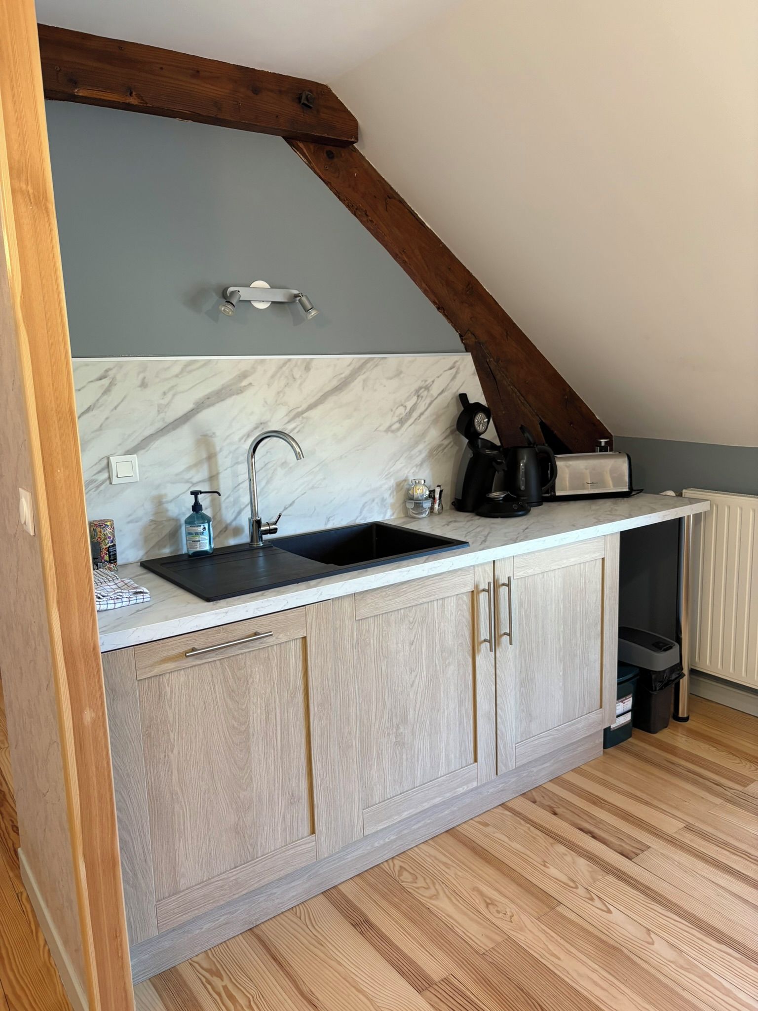 Een keuken met een marmeren achterwand, houten kastjes, een zwarte spoelbak en een koffiezetapparaat.