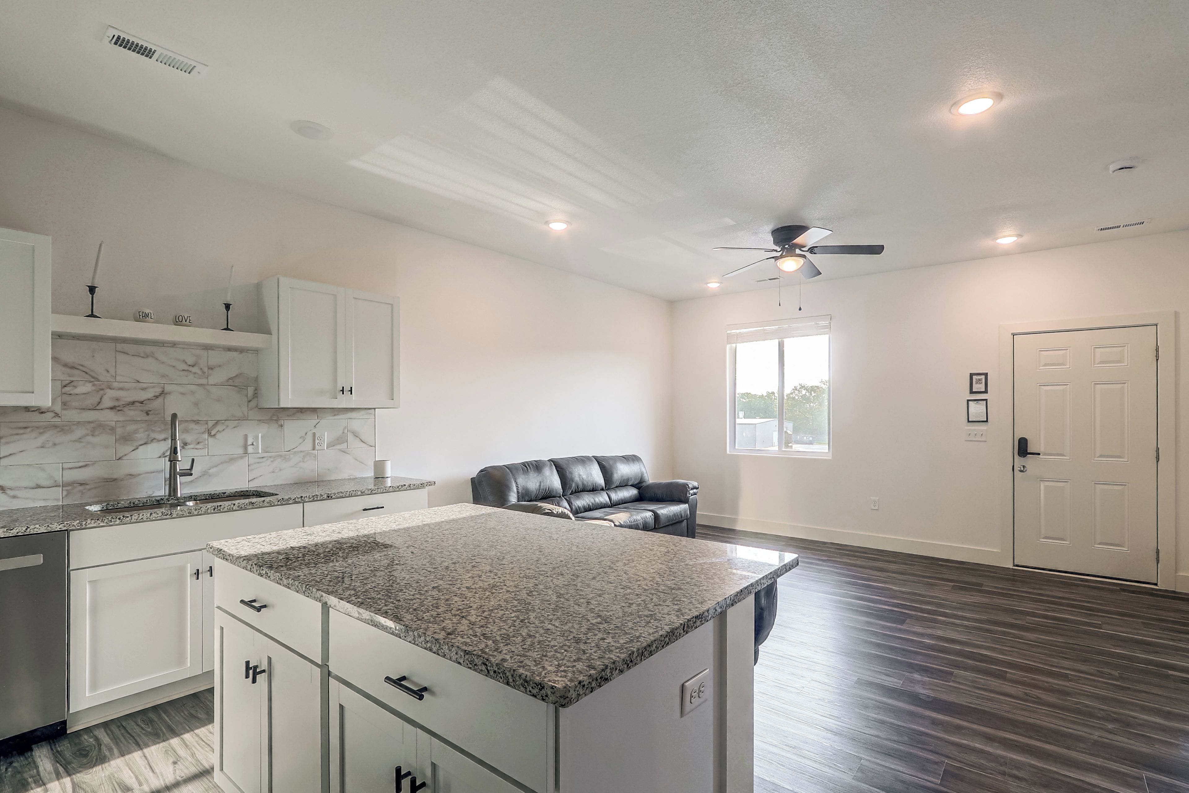 A modern kitchen with granite countertops, white cabinetry, and a marble backsplash.
