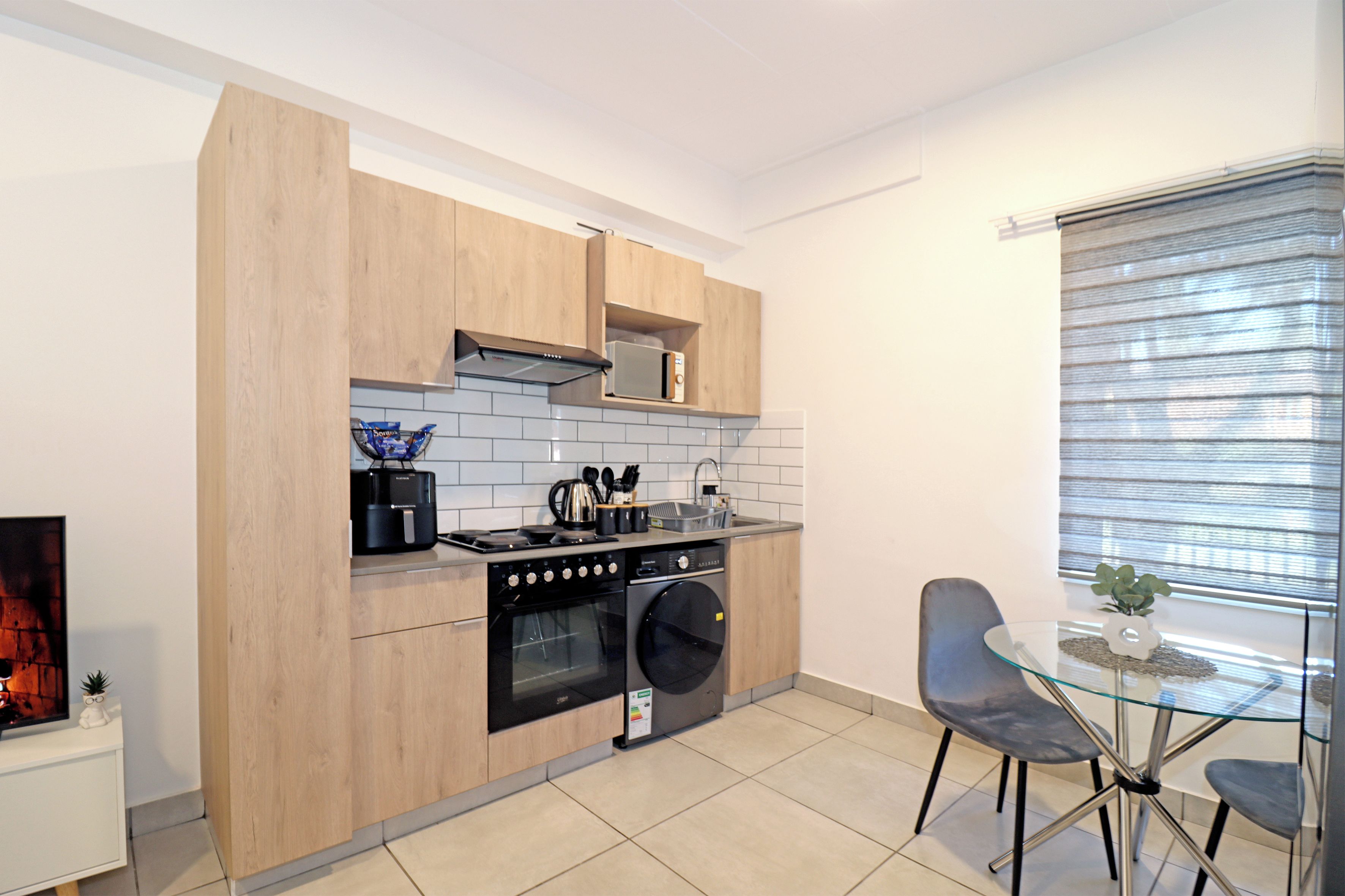 A modern kitchen with wooden cabinets, a built-in oven, a microwave, and a glass dining table with chairs.
