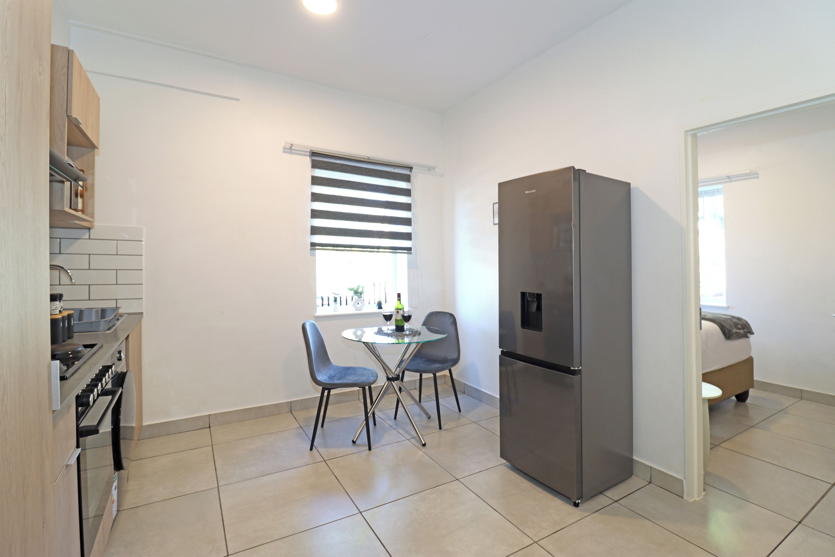 A modern kitchen with a built-in oven, a refrigerator, and a dining area with two chairs and a small table.