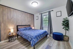 A bedroom with a bed, a bedside table, a lamp, a window with curtains, a plant, and a TV on the wall. - Poconos Mtn Getaway: 4 Mi to Camelback Resort (Tannersville)