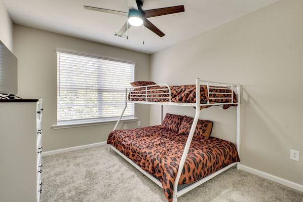 A bunk bed with a leopard print bedspread, a ceiling fan, a window with blinds, and a carpeted floor.