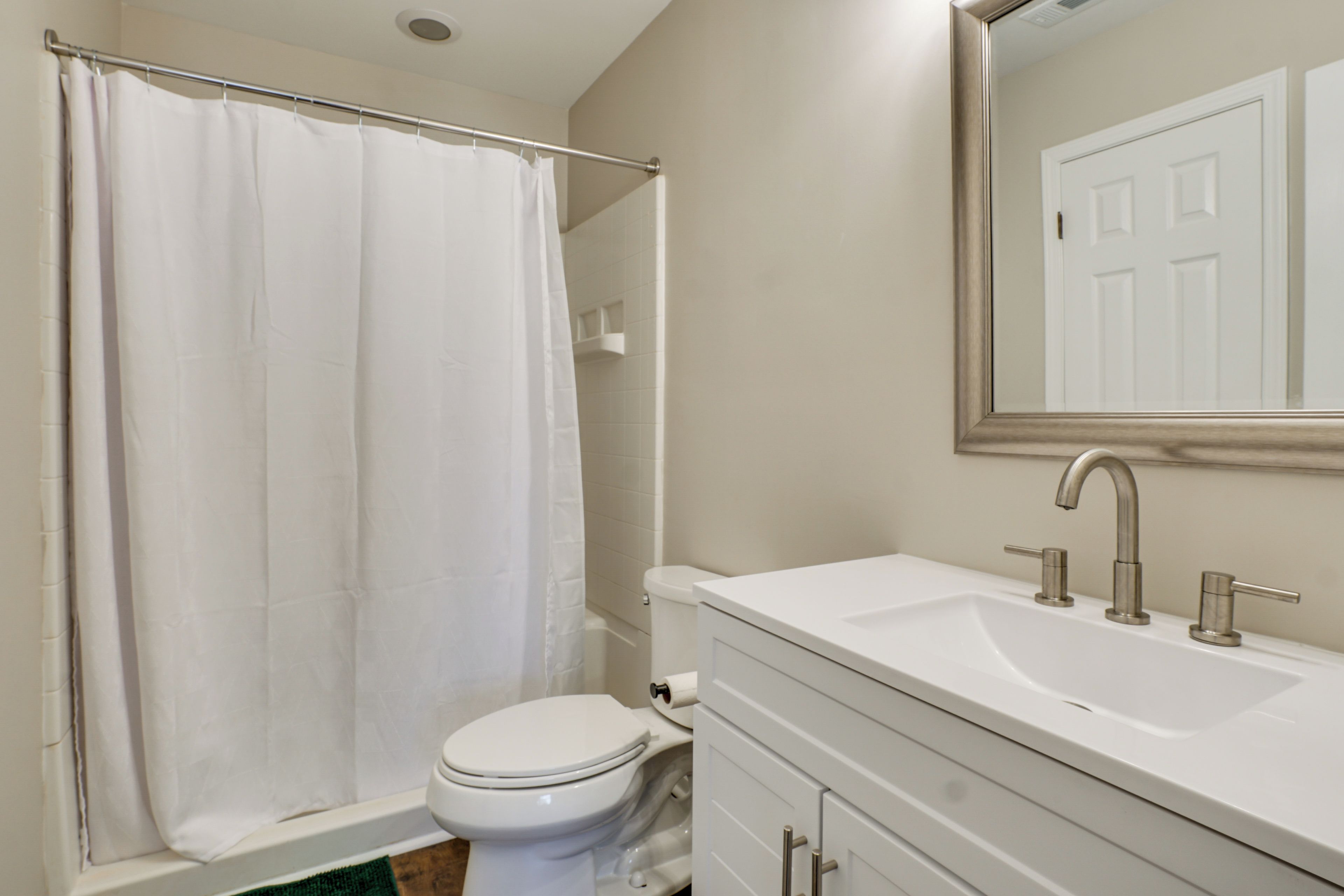 A bathroom with a white toilet, a bathtub with a shower curtain, a sink with a mirror above it, and a door in the background.
