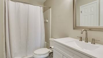 A bathroom with a white toilet, a bathtub with a shower curtain, a sink with a mirror above it, and a door in the background.