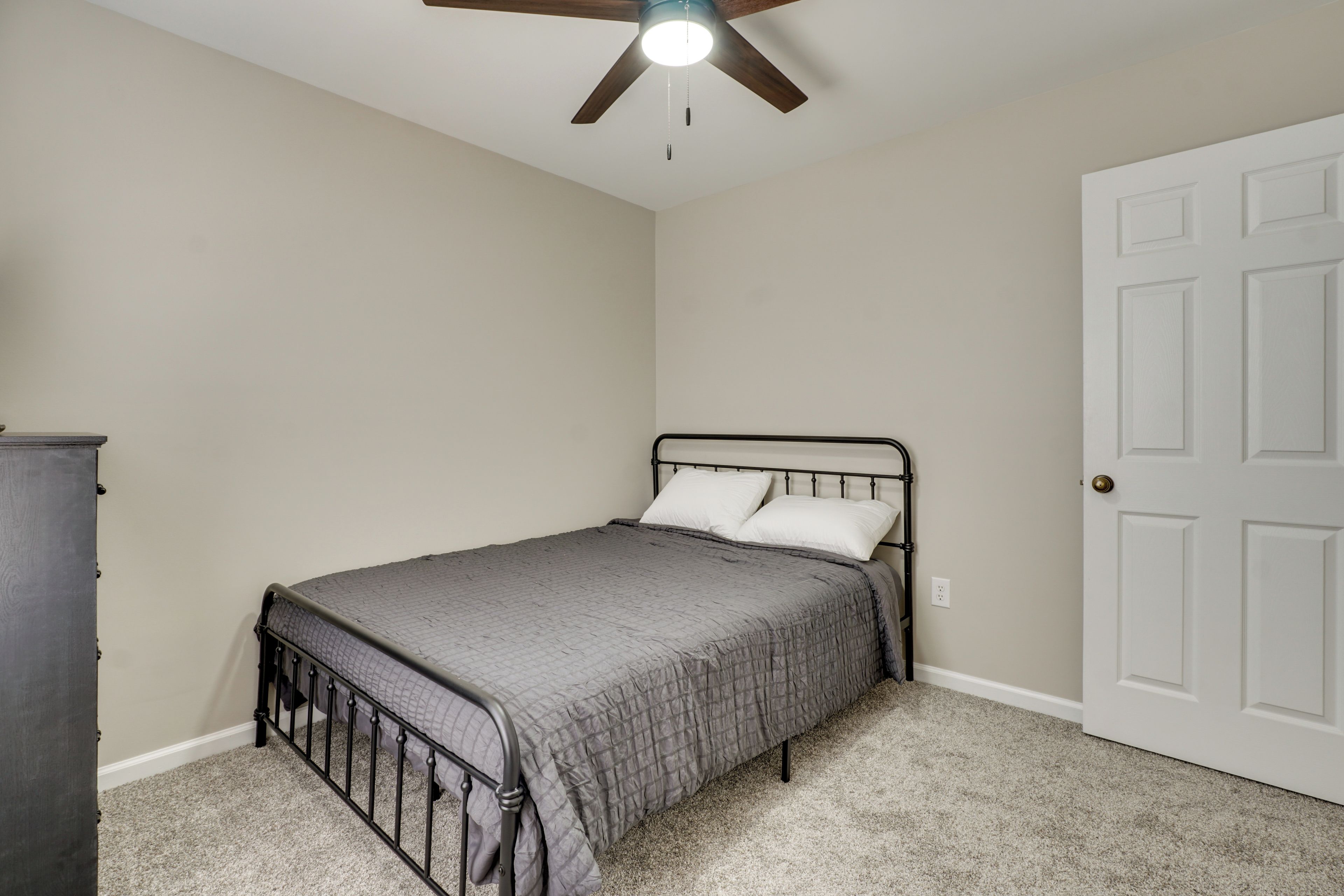 A bedroom with a bed, a ceiling fan, a door, and a dresser.