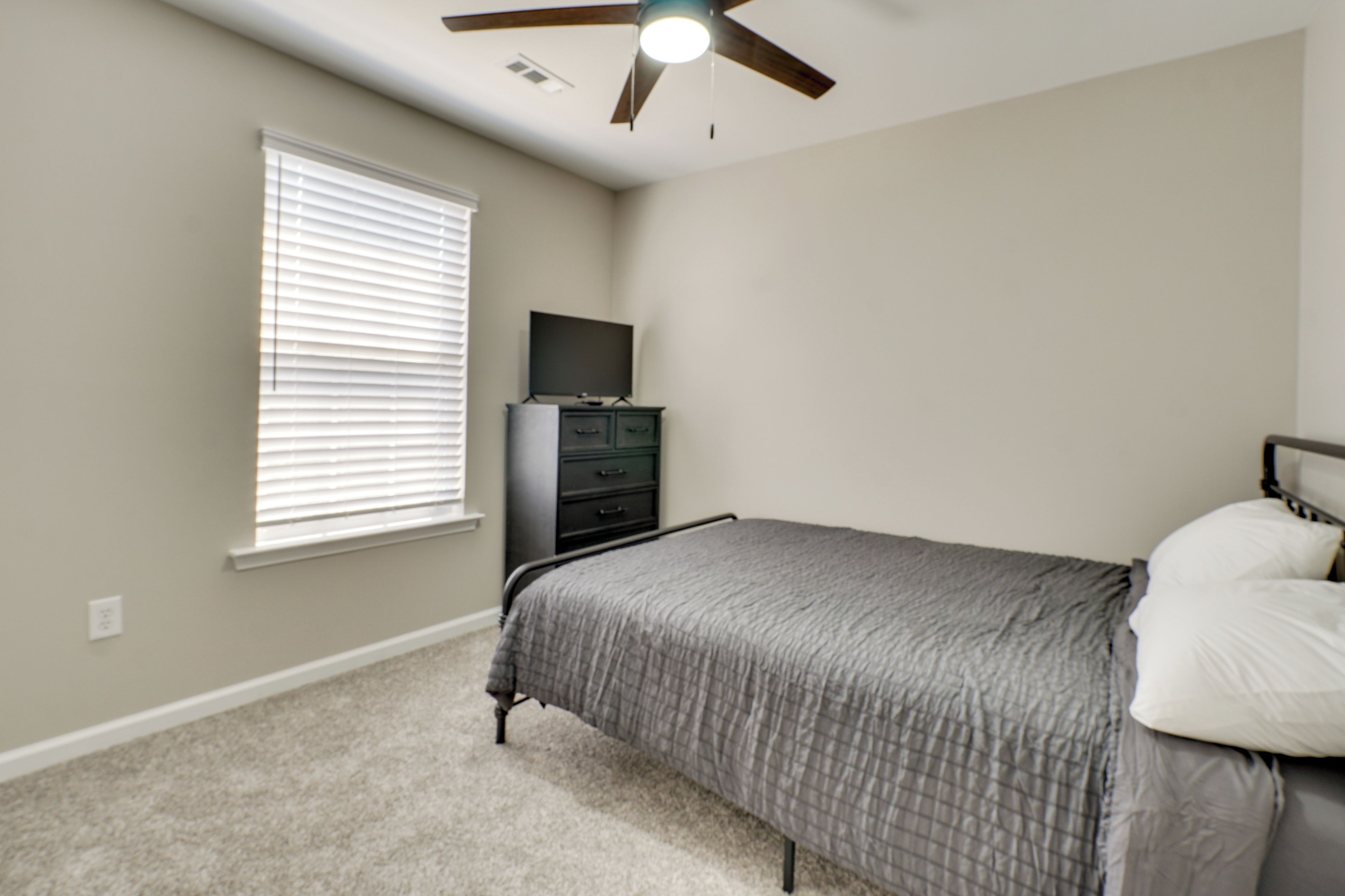 A bedroom with a bed, a dresser, a television, and a ceiling fan.