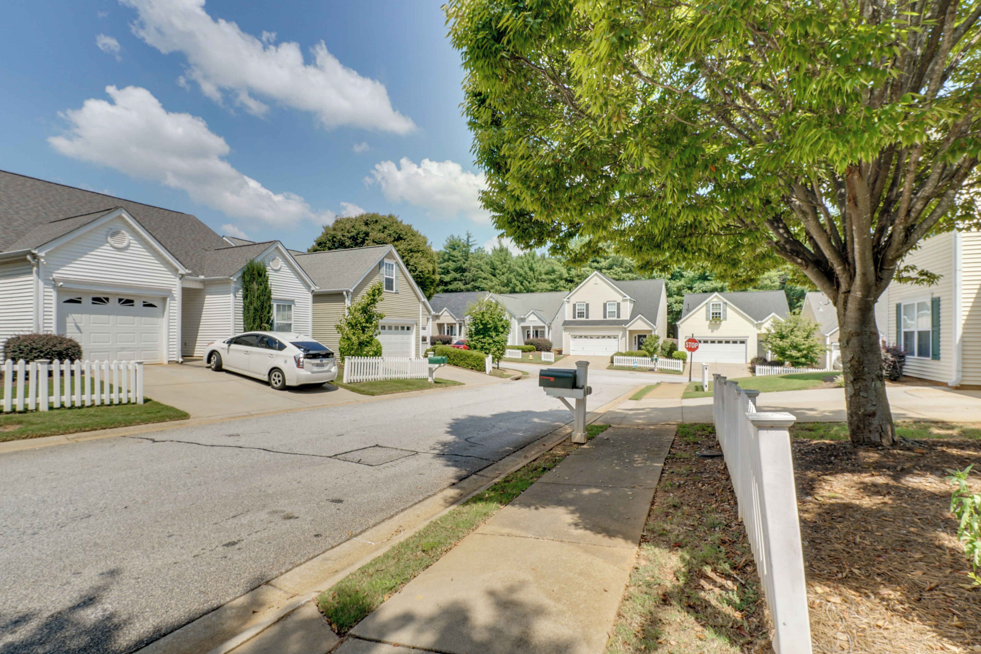 A residential street with houses, a white car parked on the street, and a mailbox.