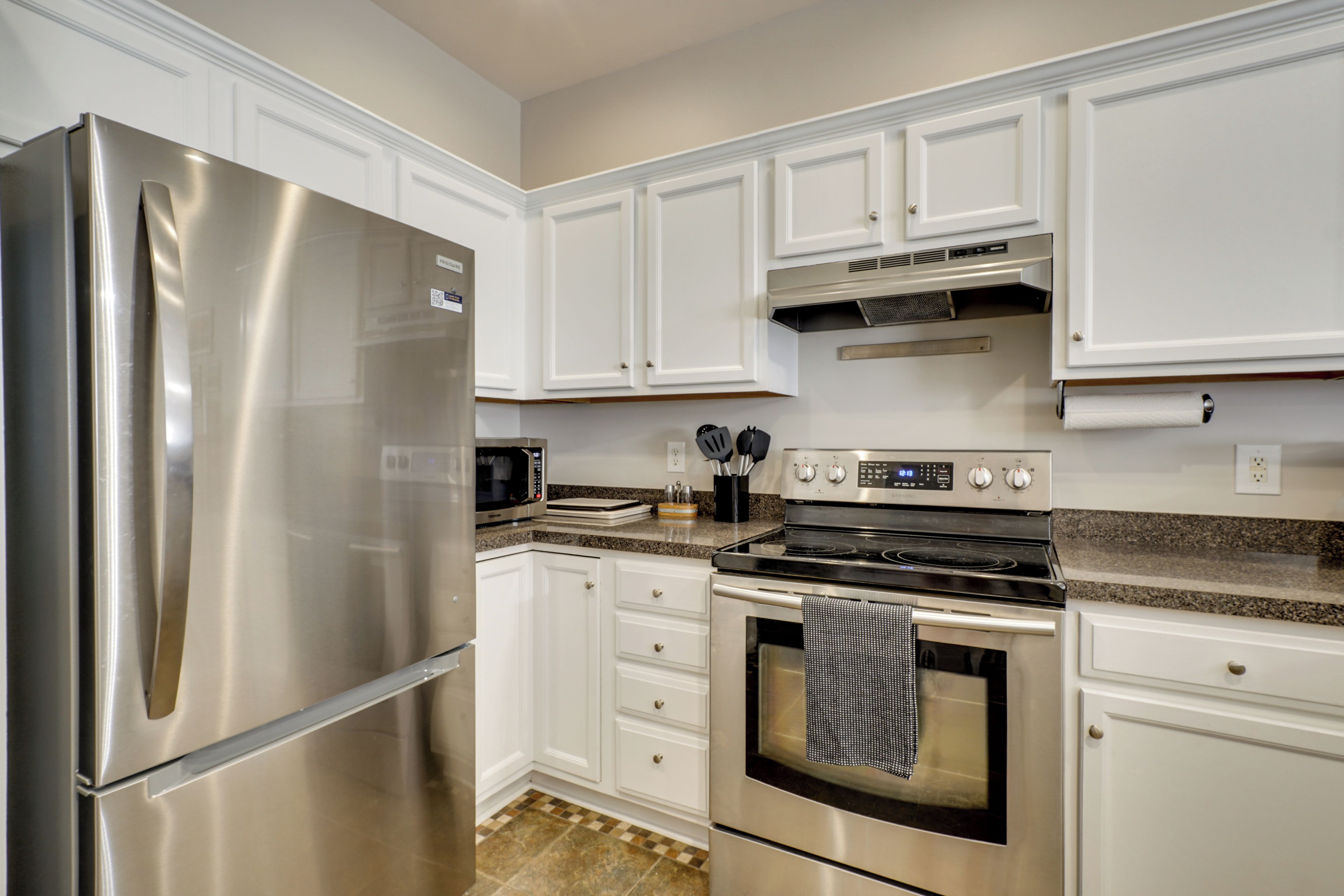 A modern kitchen with stainless steel appliances, white cabinetry, and a granite countertop.