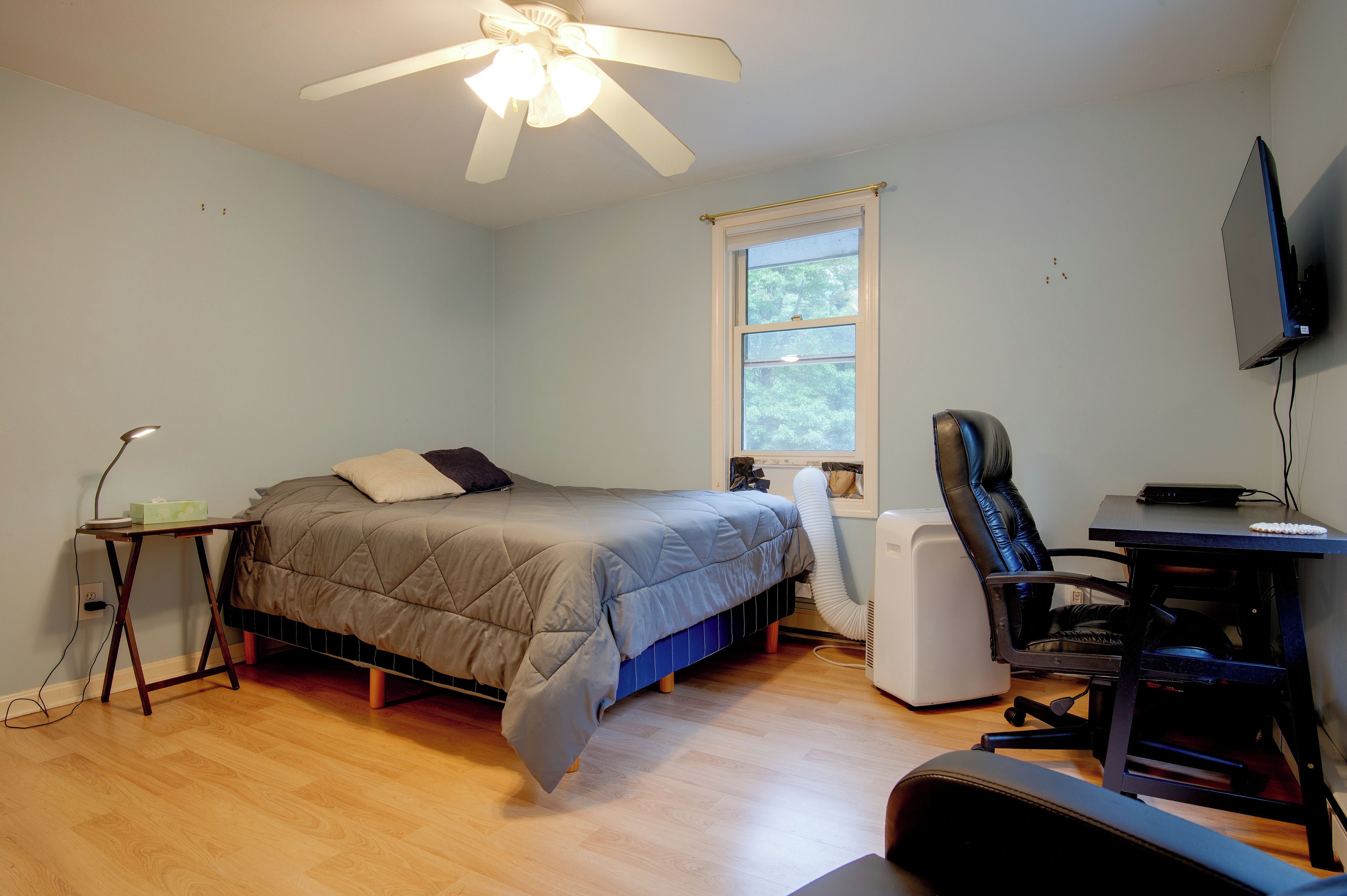 Un dormitorio con cama, escritorio, silla, ventilador de techo y ventana.