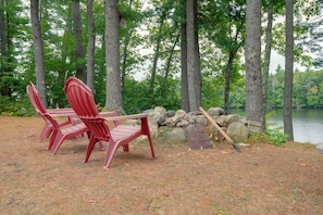 Un camping con dos sillas Adirondack, una mesa de picnic y una orilla rocosa junto a un lago.