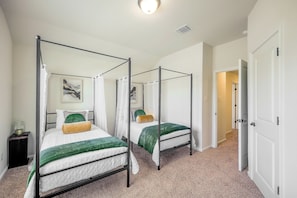 Ein Zimmer mit zwei Himmelbetten, einem Nachttisch mit Lampe und einer Tür zu einem weiteren Raum.