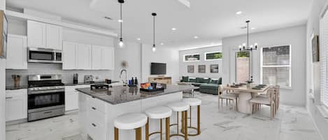 A modern kitchen with a central island, bar stools, and a dining area with a table and chairs.