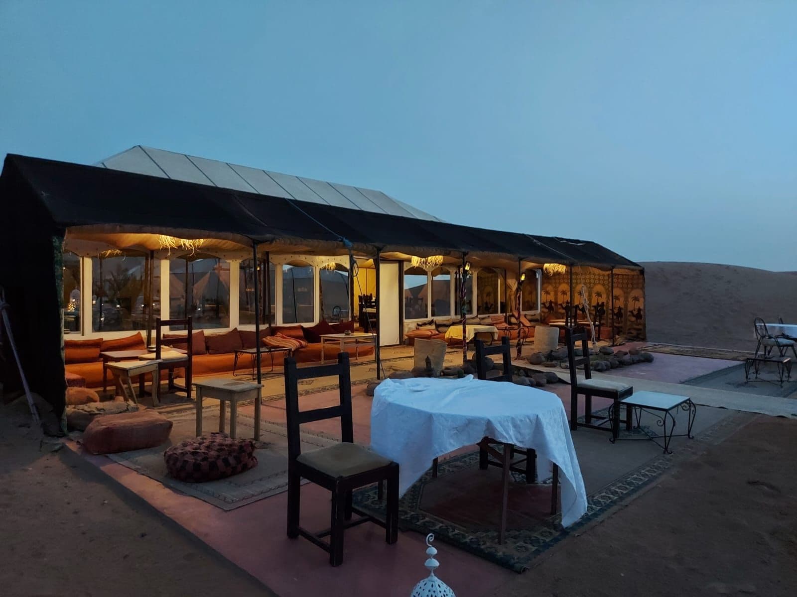 A desert tent with a dining area, sofas, and a table set for guests.