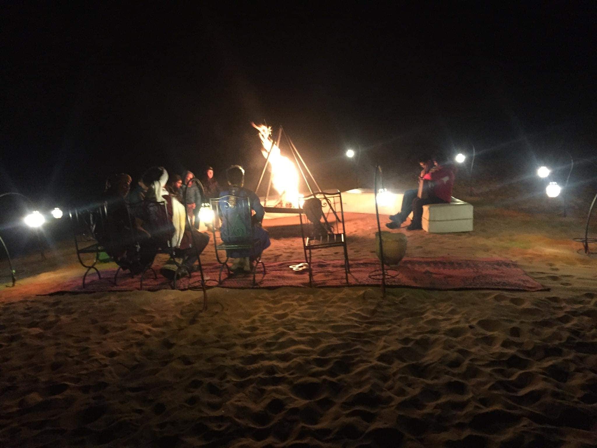 A group of people gathered around a campfire at night on a sandy beach.