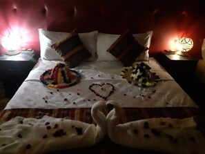A bed with a heart-shaped decoration made of rose petals and a swan-shaped decoration, a red upholstered headboard, and two bedside tables with lamps. - luxury camp sable dor (Merzouga)
