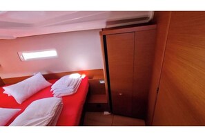 A hotel room with a bed, pillows, a nightstand, a wooden wardrobe, and a small window. - Sun Odyssey 410 - Rosso Bianco (Pula)