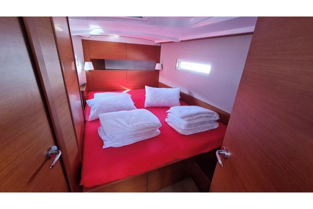 Habitación pequeña con una cama individual, una colcha roja y toallas blancas dobladas con cuidado.