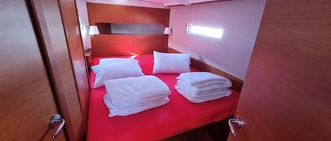 Habitación pequeña con una cama individual, una colcha roja y toallas blancas dobladas con cuidado.