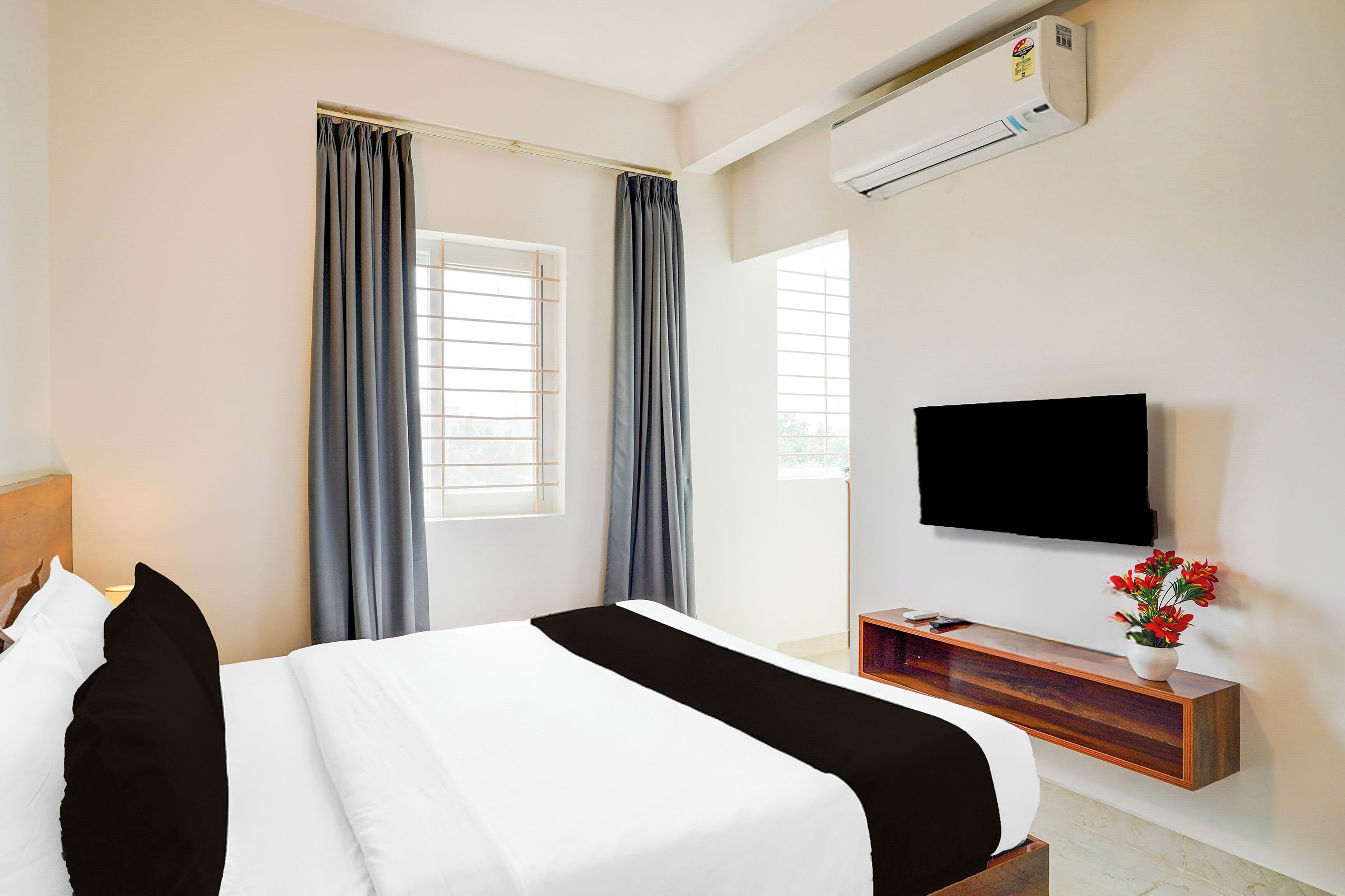 A hotel room with a bed, a TV, a window with curtains, and an air conditioning unit.