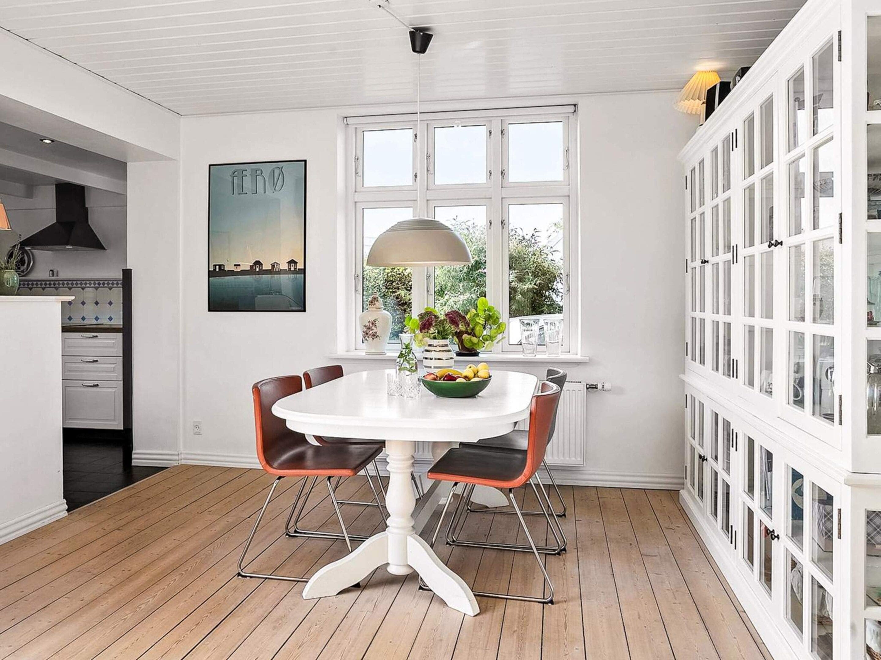 A dining area with a white table, two chairs, a window with a view, and a cabinet with glass doors.