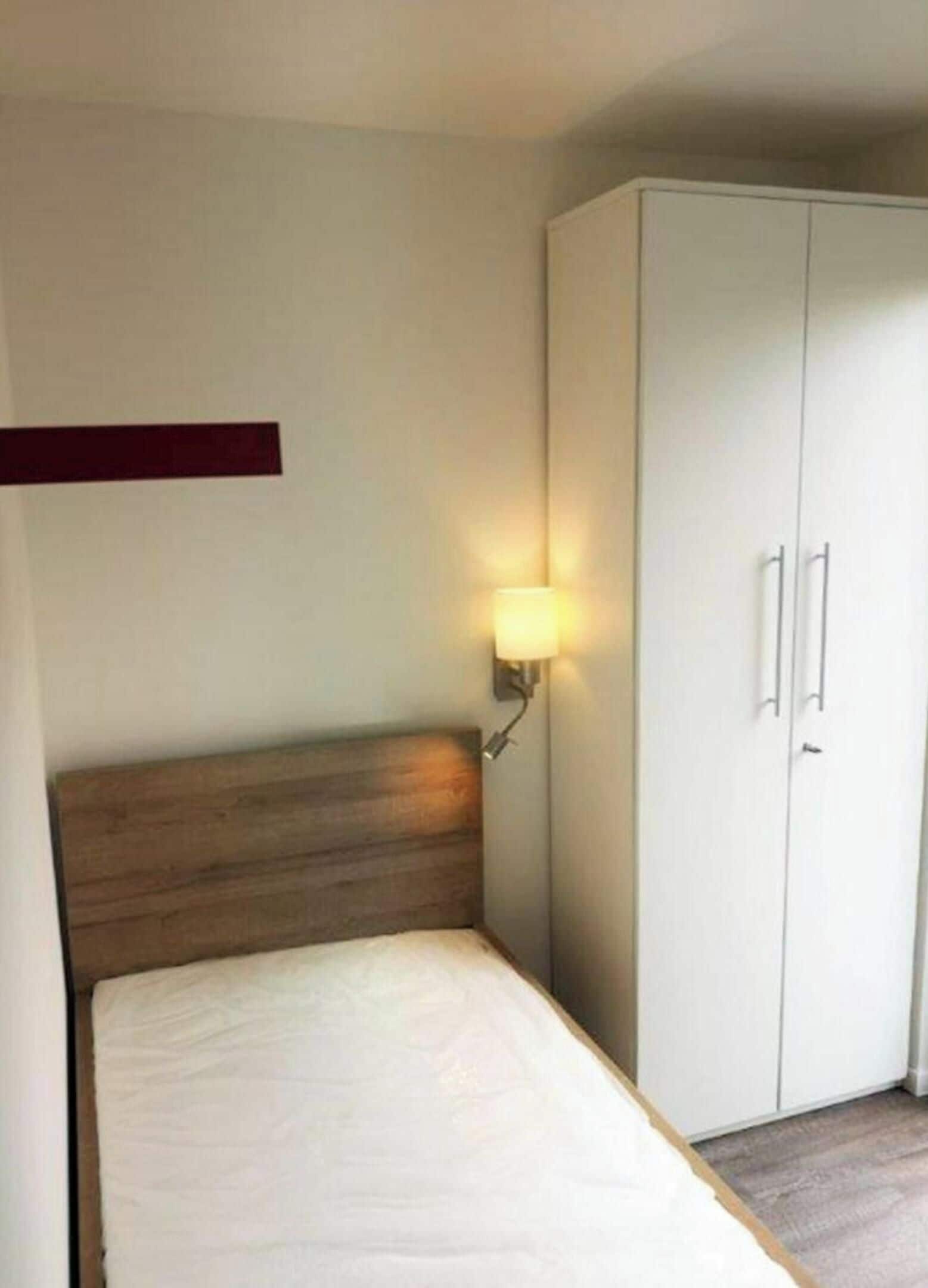 Une chambre à coucher comprenant un lit, une table de chevet, une lampe fixée au mur et une armoire.