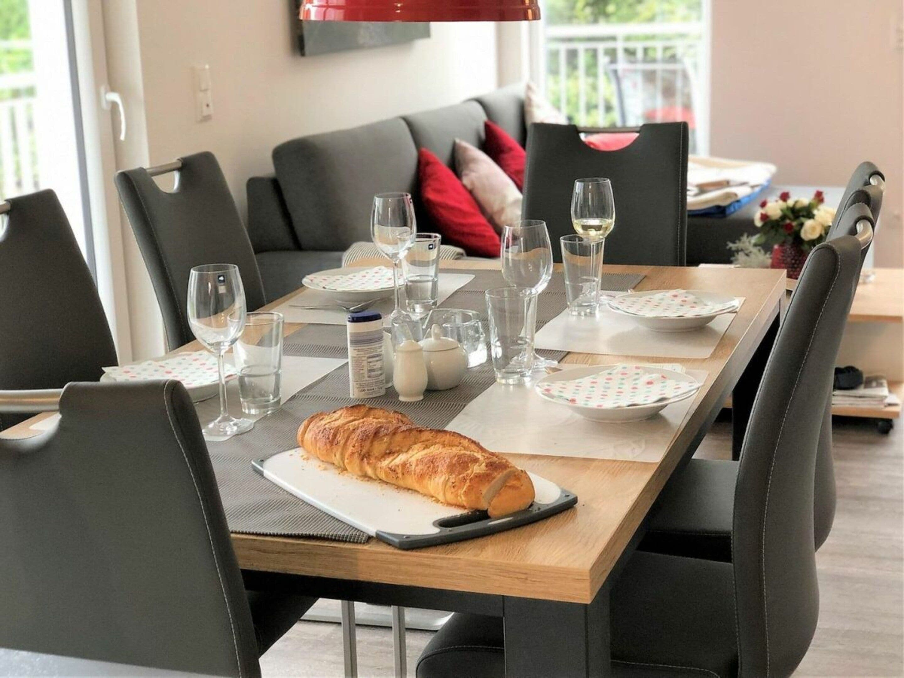A dining area with a table set for two, featuring a loaf of bread, wine glasses, and plates.