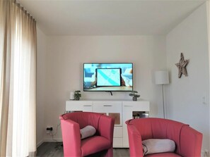 A living room with a flat-screen TV mounted above a white console, two red armchairs, a star decoration on the wall, and a floor lamp. - House No. 36, Holiday Home Deichgraf (Wangerland)