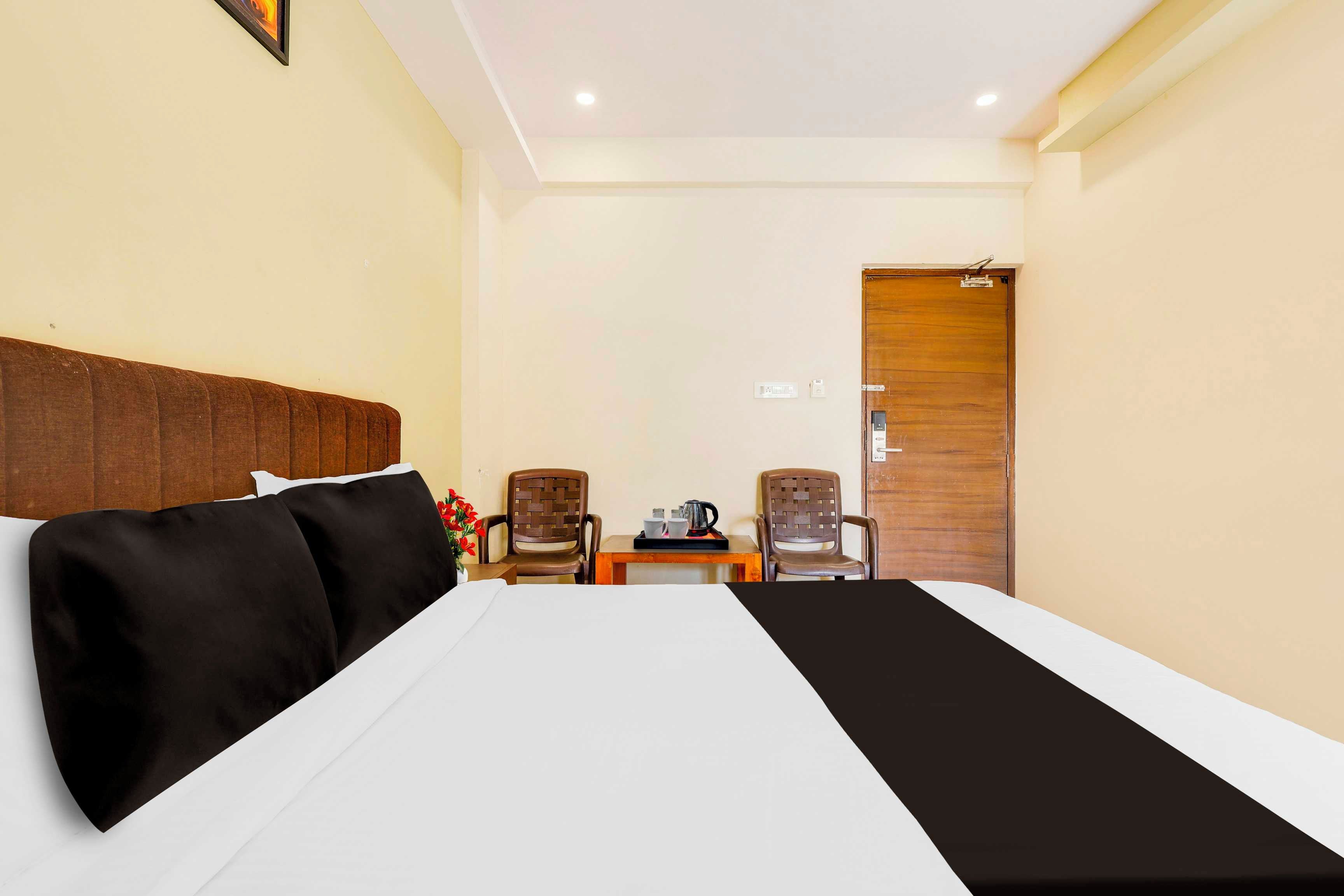 Una habitación de hotel con cama, dos sillas, una mesita con hervidor y una puerta de madera.
