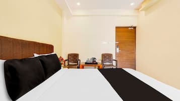Una habitación de hotel con cama, dos sillas, una mesita con hervidor y una puerta de madera.