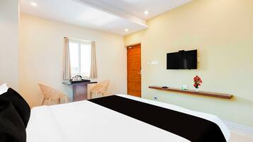 Ein Hotelzimmer mit einem Bett, einem Schreibtisch mit Stuhl, einem Fernseher und einer kleinen Ablage mit einer Vase.