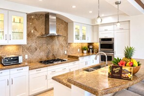 A modern kitchen with white cabinetry, granite countertops, a stainless steel range hood, and a fruit bowl on the island. - Wailea Beach Villas with Private Plunge Pool | 3 BR Sleeps 8 | Car Incl. w/ 6+ Nights | WBV-G101 by KBM (Wailea)