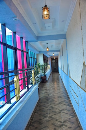 A corridor with patterned flooring, a railing with a potted plant, and a hanging light fixture.