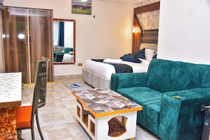 A hotel room with a bed, a green sofa, a small table, a mirror, and a wardrobe.