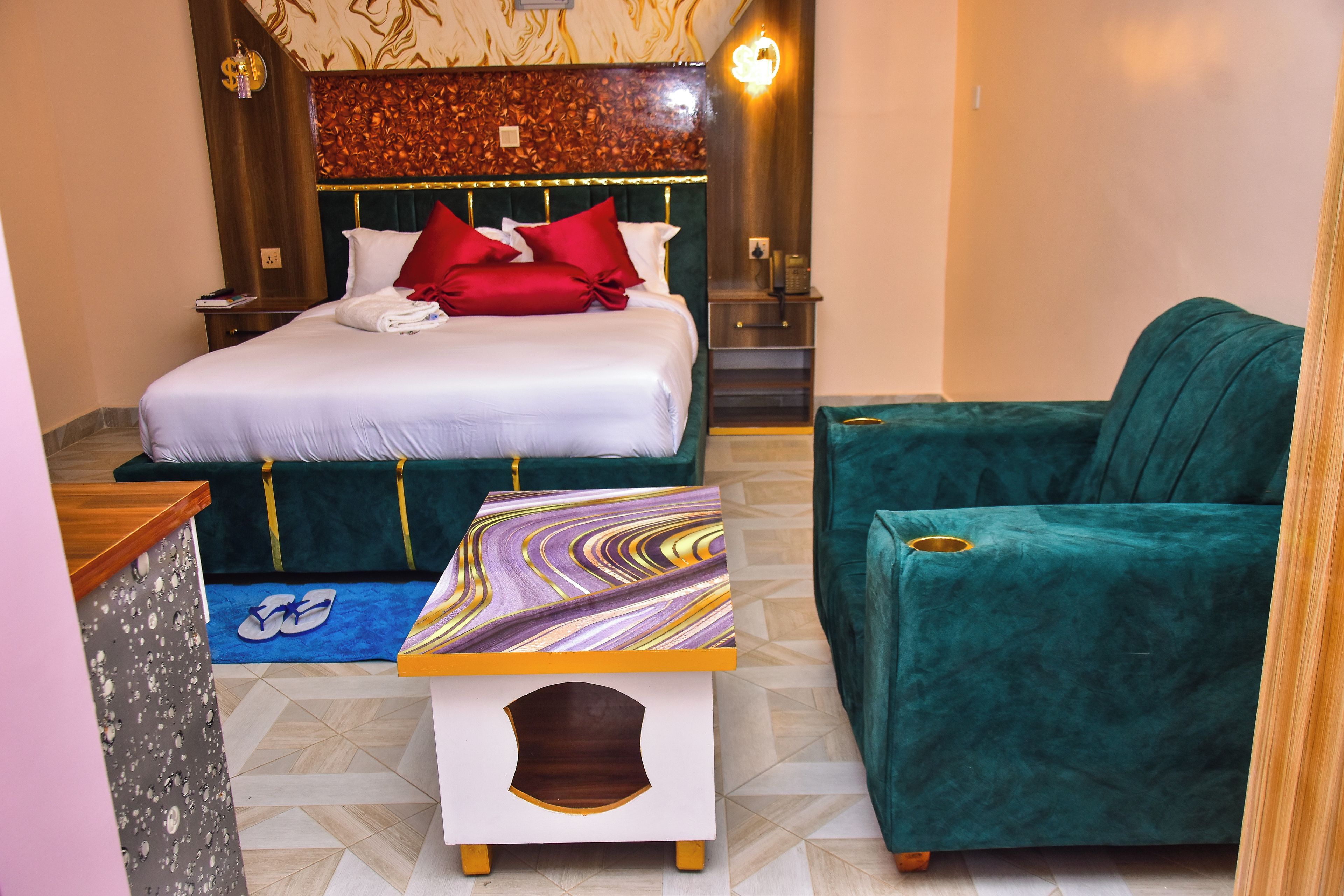 Una habitació d'hotel amb un llit, un butaca verda, una taula petita amb un objecte decoratiu i una tauleta de nit amb un telèfon.