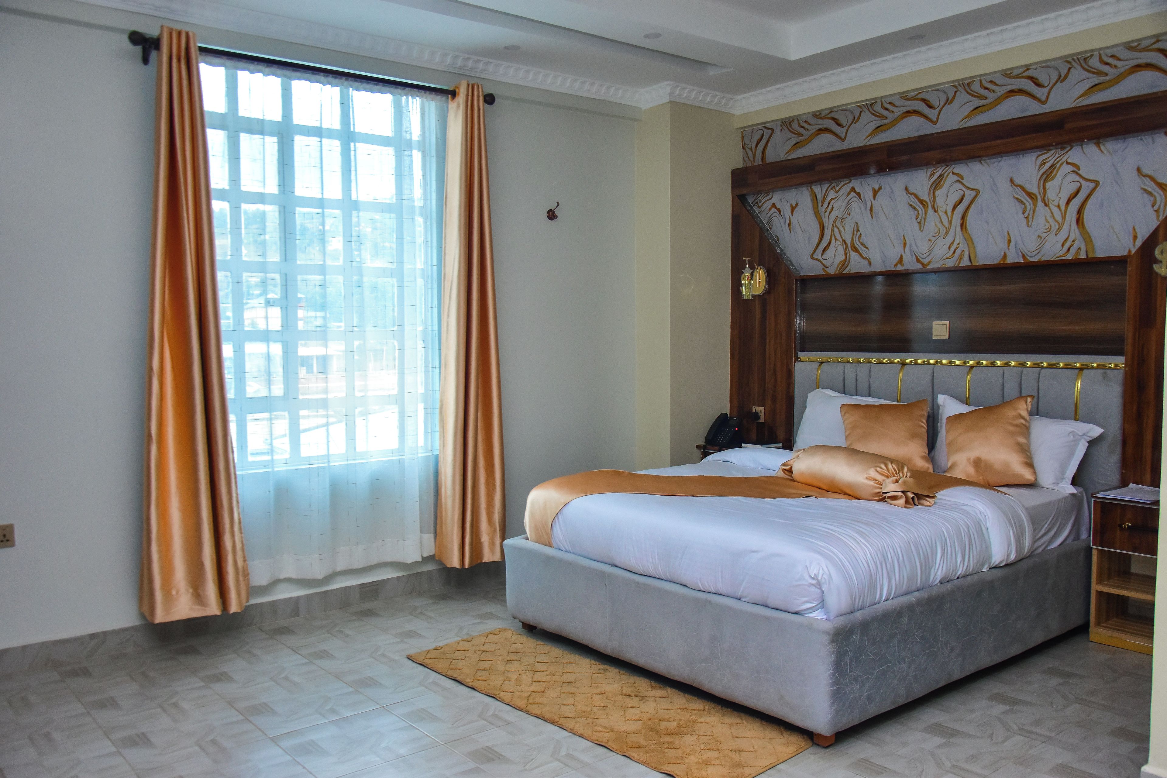 A bedroom with a bed, curtains, a headboard, a bedside table, and a telephone.