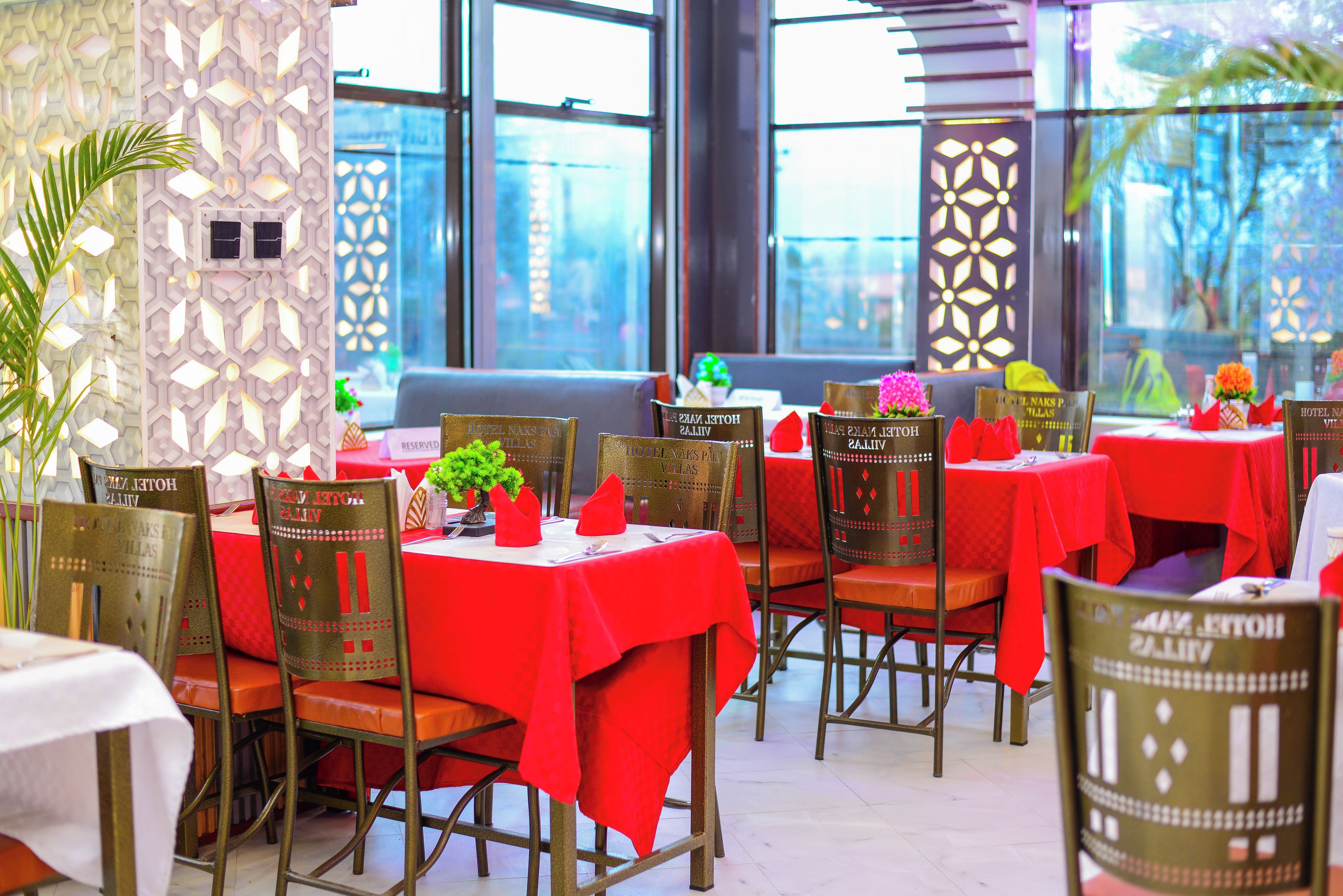 Un restaurante con mesas cubiertas por manteles rojos, sillas de diseño peculiar y vistas de la ciudad a través de amplios ventanales.