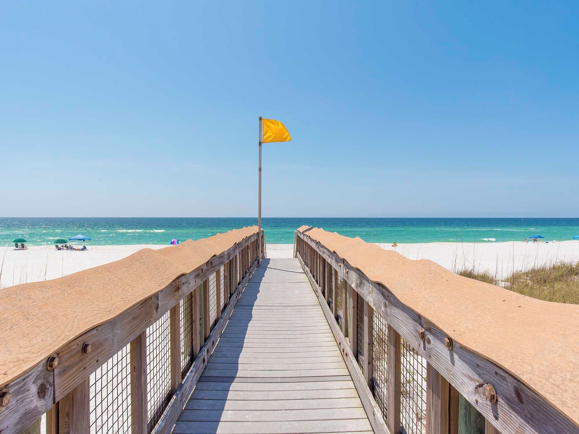 A wooden boardwalk leading to a beach with a yellow flag.