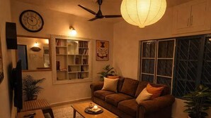 Una sala de estar acogedora con un sofá, una mesa de centro, un televisor, una estantería y una lámpara decorativa.