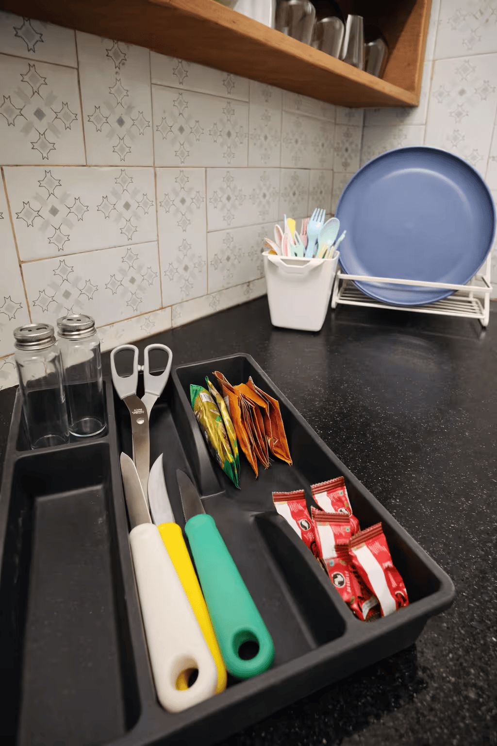 Una encimera de cocina con una bandeja que contiene varios utensilios, un plato azul y un recipiente con cubiertos.