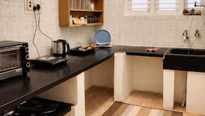 Una cocina con encimera negra, estufa, cafetera y ventana con persianas.