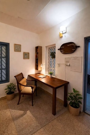 Una habitación con una mesa de madera, dos sillas, una planta en maceta y una lámpara fijada a la pared.