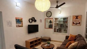 Una sala de estar con sofá, sillón, mesa de centro, estantería y televisor montado en la pared.