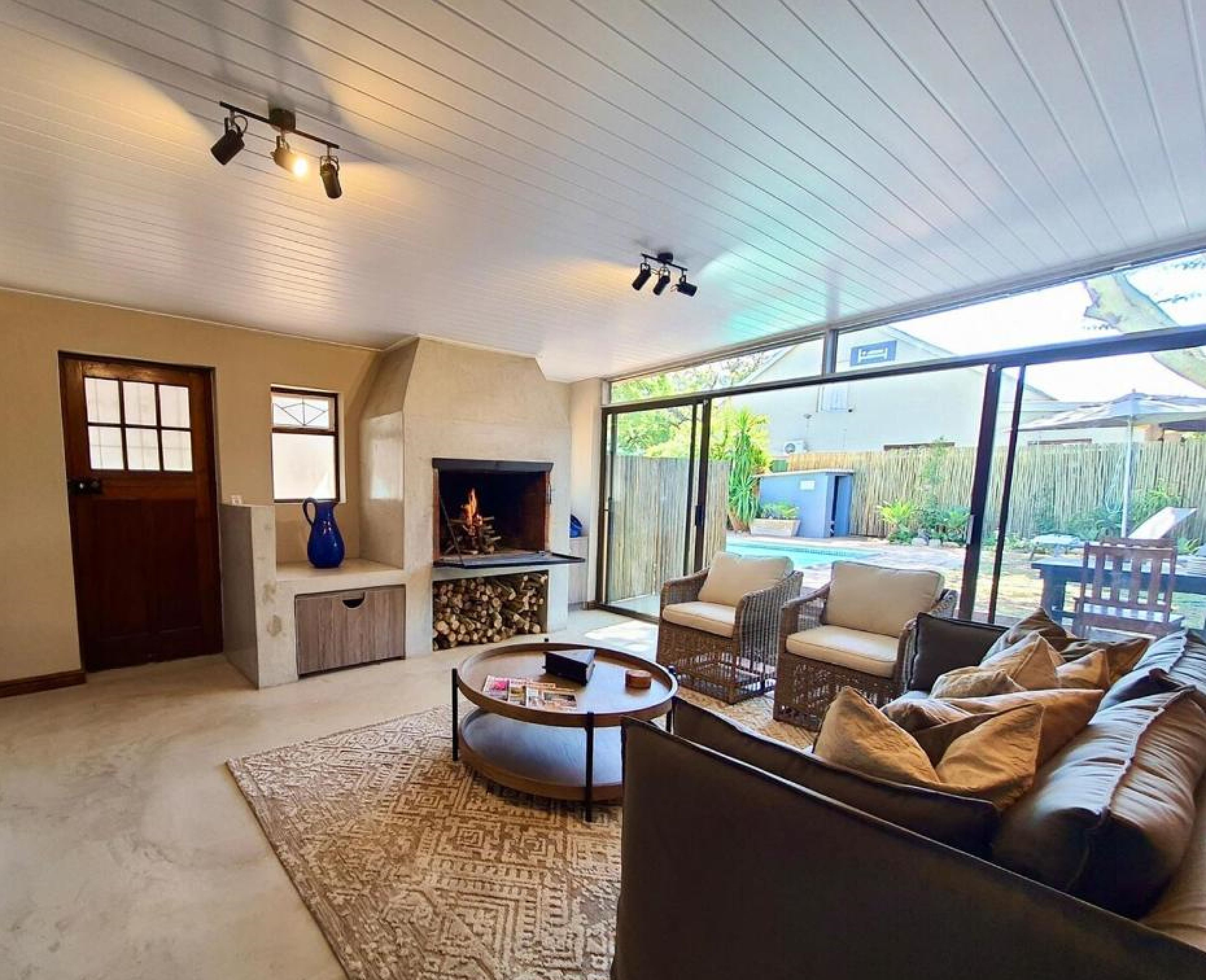 A spacious living room with a fireplace, a pool visible through large windows, and a cozy seating area.
