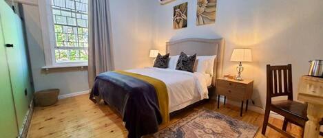 A bedroom with a bed, a nightstand, a chair, a window with curtains, and a wall-mounted air conditioner.