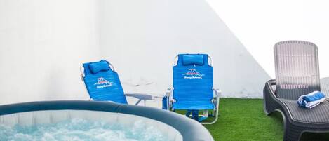 A pool area with two lounge chairs and a hot tub.