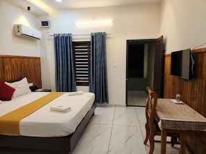 Habitación de hotel con cama, escritorio, televisor, aire acondicionado y puerta corrediza.